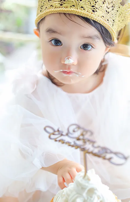 クリームだらけになりながらケーキに手を伸ばす1歳の赤ちゃん