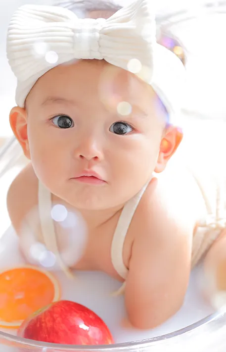 ミルクバスのお湯につかりフルーツに囲まれた赤ちゃんの表情