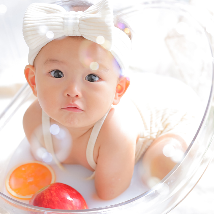 花を浮かべた乳白色のお湯に入る赤ちゃんのミルクバス撮影