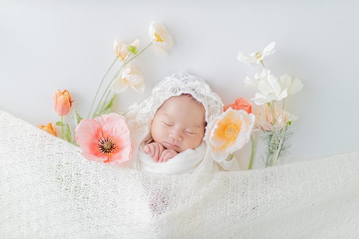 花に囲まれておくるみに包まれた新生児のニューボーンフォト
